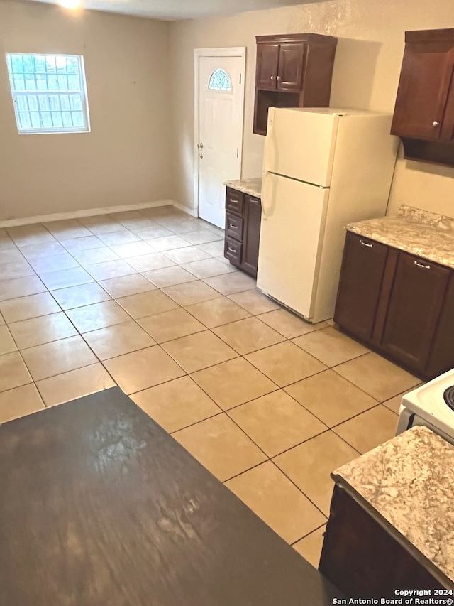 kitchen with dark brown cabinets, white refrigerator, light tile patterned floors, and light stone counters