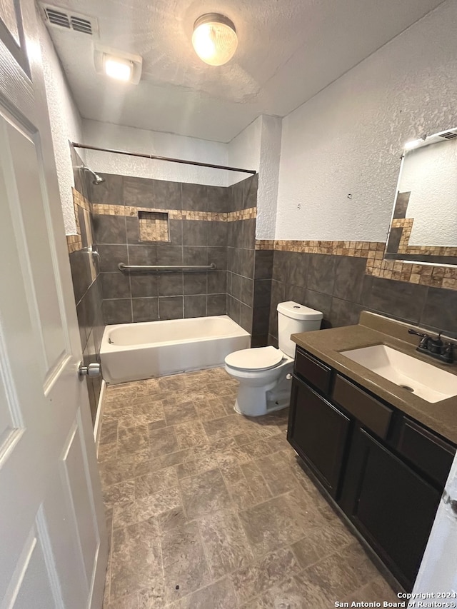 full bathroom with tile walls, toilet, tile patterned floors, vanity, and tiled shower / bath combo