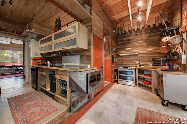 kitchen with wooden walls, wooden ceiling, appliances with stainless steel finishes, beam ceiling, and light tile patterned flooring