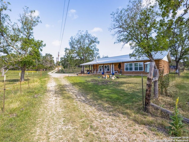 view of front of house with metal roof, a porch, driveway, log exterior, and a front lawn