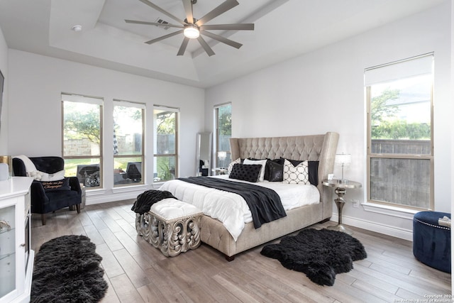 bedroom featuring ceiling fan, light hardwood / wood-style flooring, and a tray ceiling