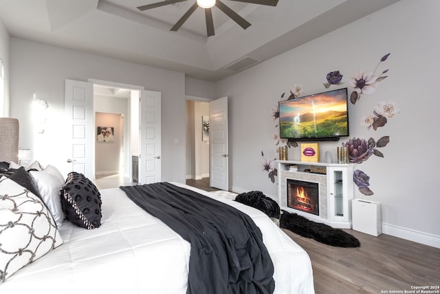 bedroom with hardwood / wood-style floors, a raised ceiling, ceiling fan, and a stone fireplace