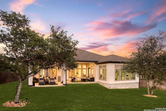 back house at dusk with an outdoor living space, a patio area, and a lawn