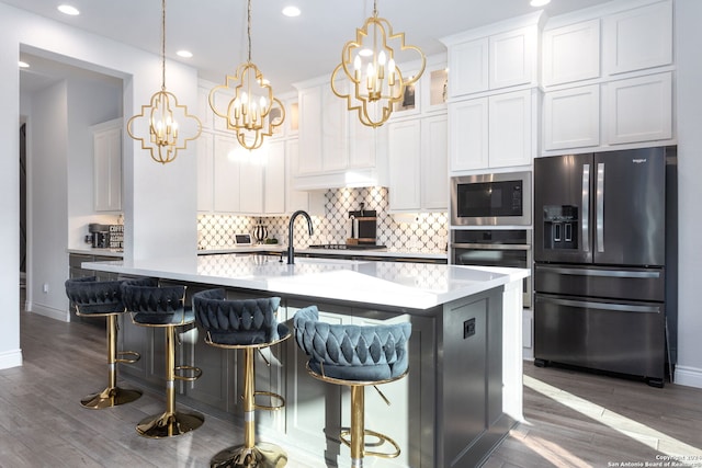 kitchen with stainless steel appliances, a kitchen breakfast bar, an island with sink, decorative light fixtures, and white cabinets