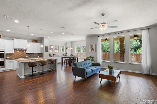 living room featuring dark hardwood / wood-style flooring, ceiling fan, and a textured ceiling