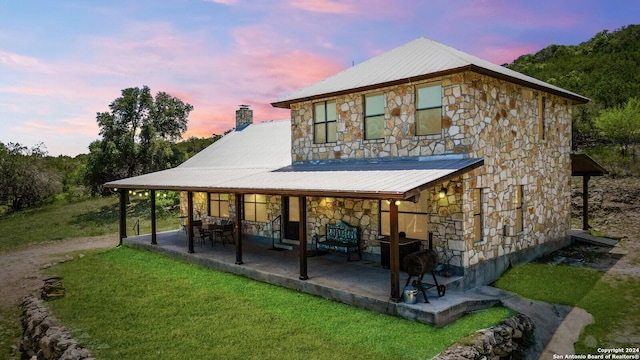 back house at dusk with a patio area and a lawn