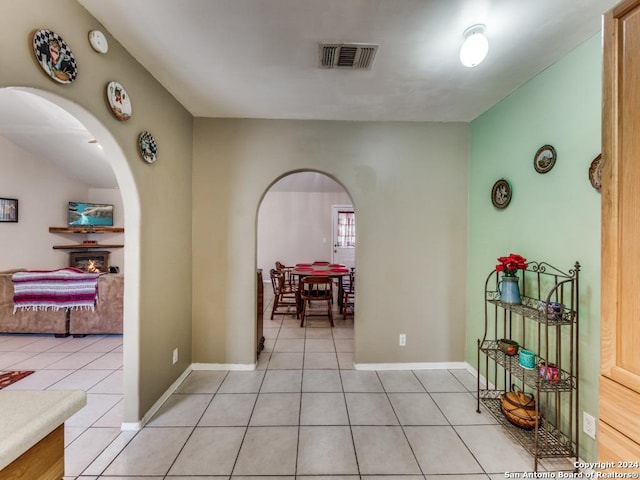 hallway featuring light tile patterned floors, baseboards, visible vents, and arched walkways