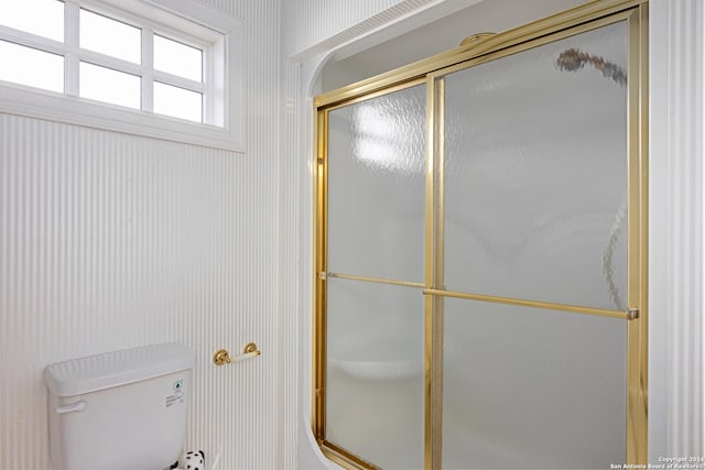 bathroom featuring a shower with door and toilet