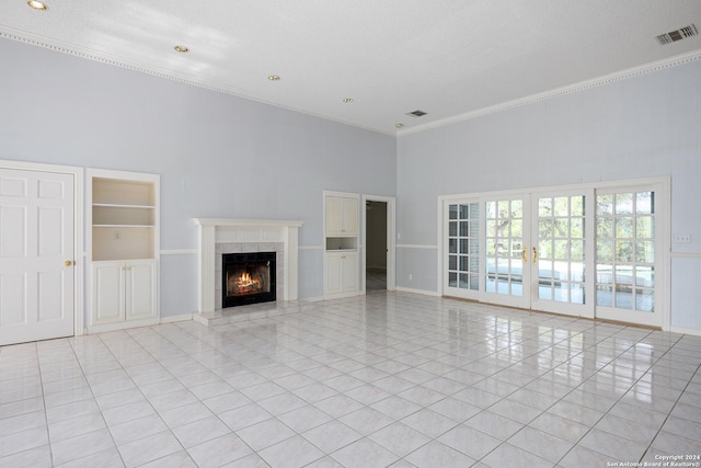 unfurnished living room with a tile fireplace, a high ceiling, ornamental molding, light tile patterned flooring, and french doors