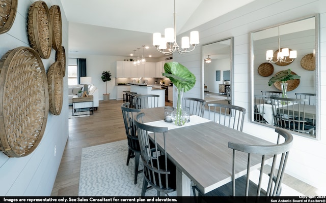 dining space featuring ceiling fan with notable chandelier, vaulted ceiling, and light hardwood / wood-style flooring