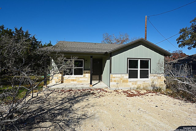 view of front of home featuring stone siding, board and batten siding, a patio, and roof with shingles