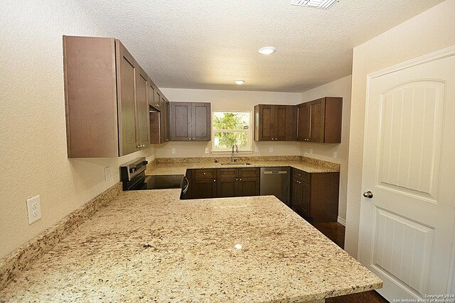 kitchen featuring a textured ceiling, a peninsula, a sink, dark brown cabinets, and appliances with stainless steel finishes