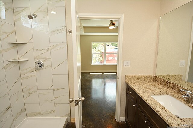 bathroom with baseboards, tiled shower, and vanity