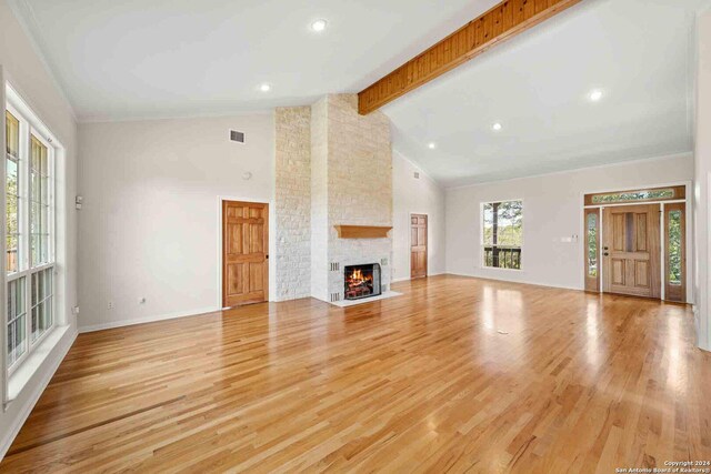 unfurnished living room featuring beamed ceiling, light hardwood / wood-style floors, brick wall, a fireplace, and high vaulted ceiling