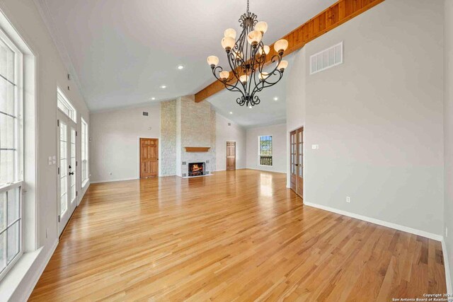 unfurnished living room with beam ceiling, a notable chandelier, light hardwood / wood-style flooring, french doors, and a fireplace