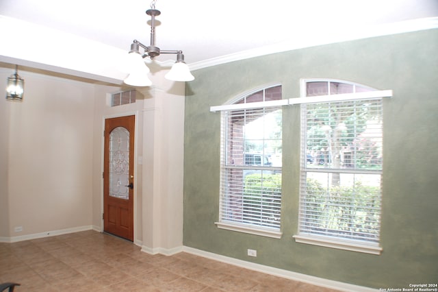 entryway with tile patterned floors, crown molding, and an inviting chandelier