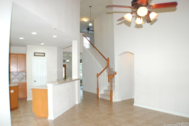 kitchen with tasteful backsplash, pendant lighting, light tile patterned floors, ceiling fan, and a towering ceiling