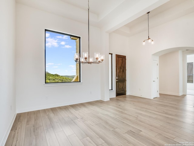 unfurnished room featuring a high ceiling, light wood-type flooring, a tray ceiling, and a chandelier