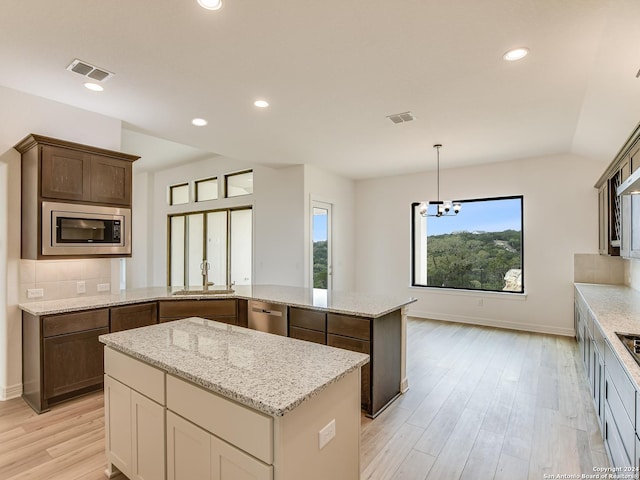 kitchen with decorative light fixtures, backsplash, kitchen peninsula, light hardwood / wood-style flooring, and stainless steel appliances