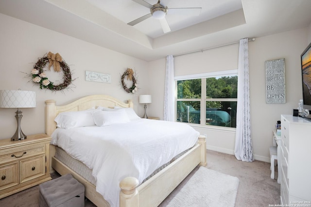 carpeted bedroom with a raised ceiling and ceiling fan