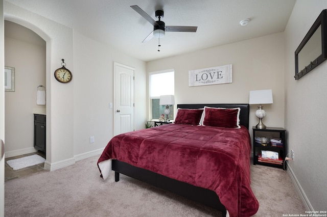 bedroom featuring light colored carpet, ensuite bath, and ceiling fan