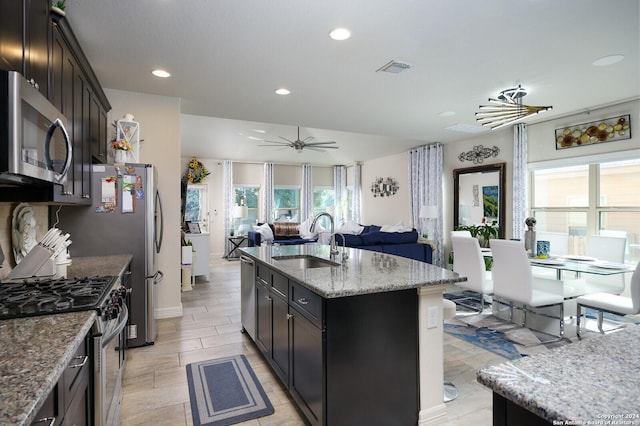 kitchen featuring appliances with stainless steel finishes, light stone counters, a kitchen island with sink, and sink