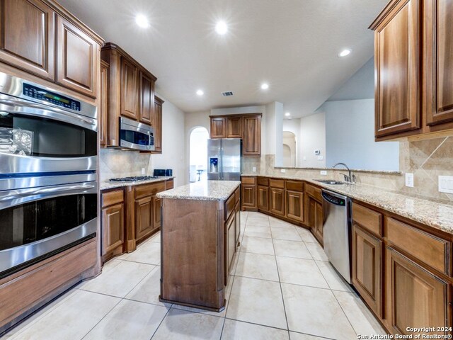 kitchen with light tile patterned floors, appliances with stainless steel finishes, light stone countertops, and a sink