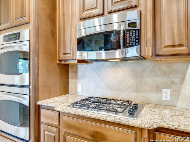 kitchen featuring light stone counters, brown cabinetry, backsplash, and stainless steel appliances