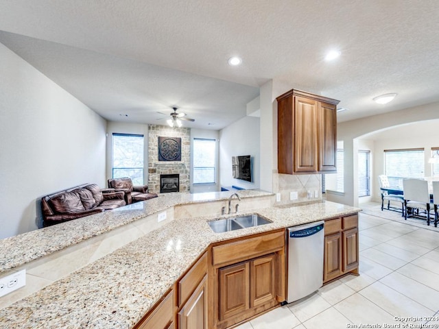 kitchen with brown cabinets, a sink, stainless steel dishwasher, open floor plan, and a fireplace