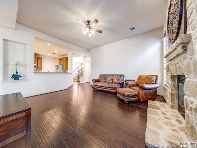 living room featuring ceiling fan, a stone fireplace, and dark wood-type flooring