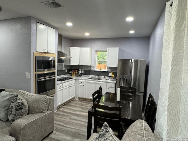 kitchen featuring white cabinetry, sink, stainless steel appliances, wall chimney range hood, and tasteful backsplash