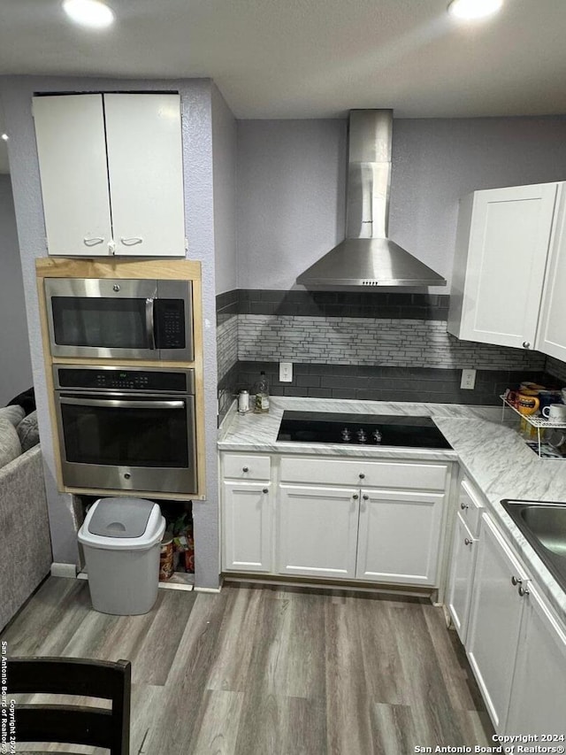 kitchen with backsplash, white cabinets, wall chimney range hood, and appliances with stainless steel finishes