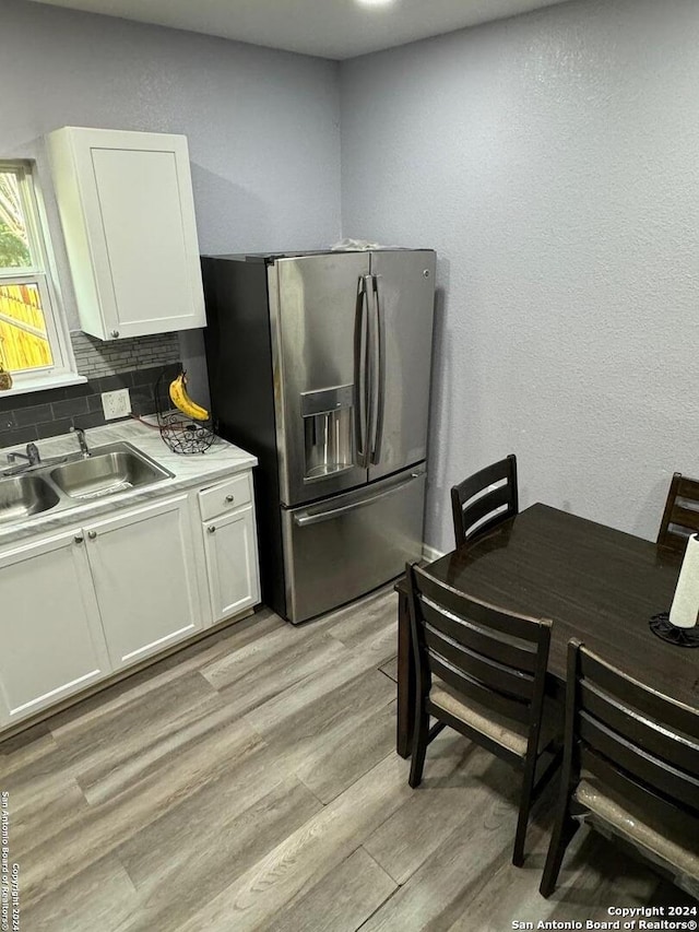 kitchen featuring sink, stainless steel refrigerator with ice dispenser, light wood-type flooring, tasteful backsplash, and white cabinetry