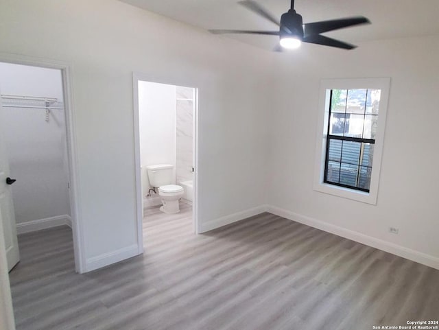 unfurnished bedroom featuring ensuite bathroom, a closet, hardwood / wood-style flooring, a walk in closet, and ceiling fan