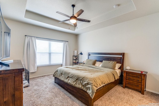 bedroom with a raised ceiling, ceiling fan, and light colored carpet