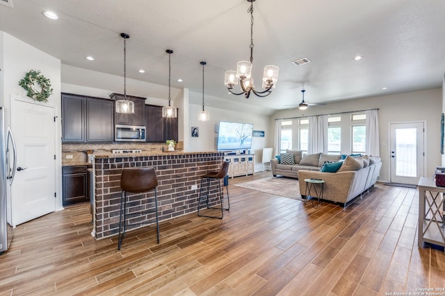 kitchen featuring a kitchen breakfast bar, ceiling fan with notable chandelier, decorative light fixtures, dark brown cabinets, and stainless steel appliances