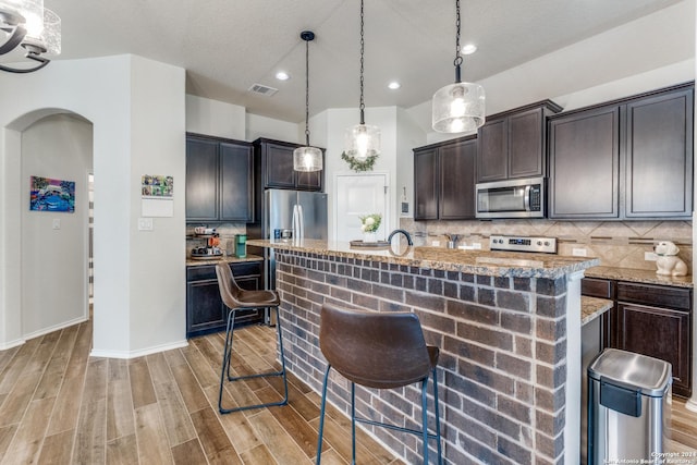 kitchen featuring a kitchen bar, dark brown cabinetry, a kitchen island with sink, and appliances with stainless steel finishes