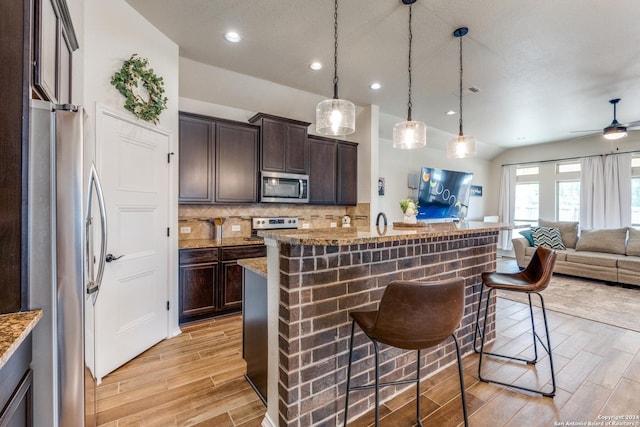 kitchen with dark brown cabinets, a kitchen bar, backsplash, and appliances with stainless steel finishes