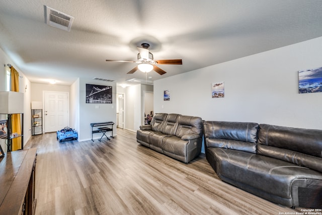 living room with a textured ceiling, light wood-type flooring, and ceiling fan