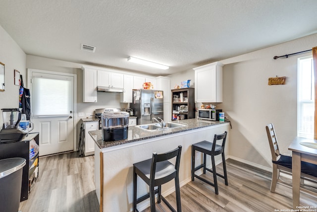 kitchen with stone counters, white cabinetry, light wood-type flooring, and stainless steel appliances