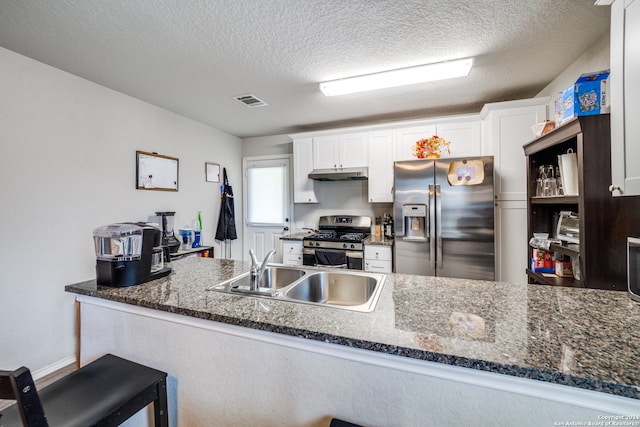 kitchen with white cabinetry, stainless steel appliances, sink, dark stone countertops, and a textured ceiling