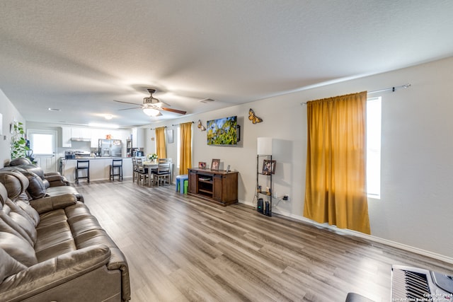 living room featuring wood-type flooring, a textured ceiling, and ceiling fan