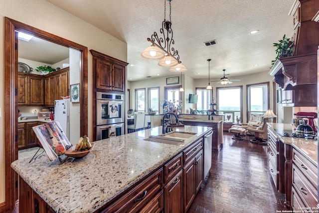 kitchen featuring light stone counters, stainless steel appliances, a spacious island, sink, and hanging light fixtures