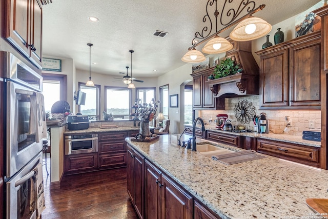 kitchen with pendant lighting, decorative backsplash, light stone countertops, and dark wood-type flooring