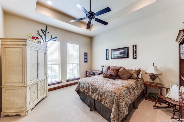 bedroom with a raised ceiling, ceiling fan, and light colored carpet