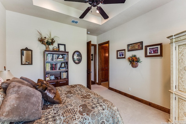 carpeted bedroom with ceiling fan and a tray ceiling