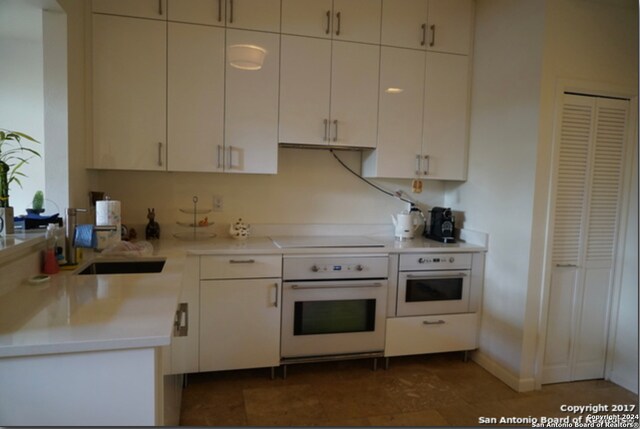 kitchen featuring stovetop, sink, white oven, and white cabinets