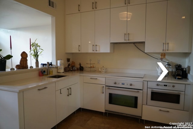 kitchen featuring stovetop, dark tile patterned flooring, oven, and sink