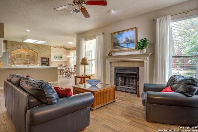 living room with a textured ceiling, light wood-type flooring, and ceiling fan