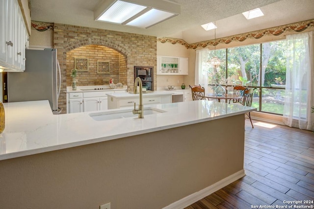 kitchen with a textured ceiling, white cabinets, hardwood / wood-style floors, stainless steel fridge, and sink